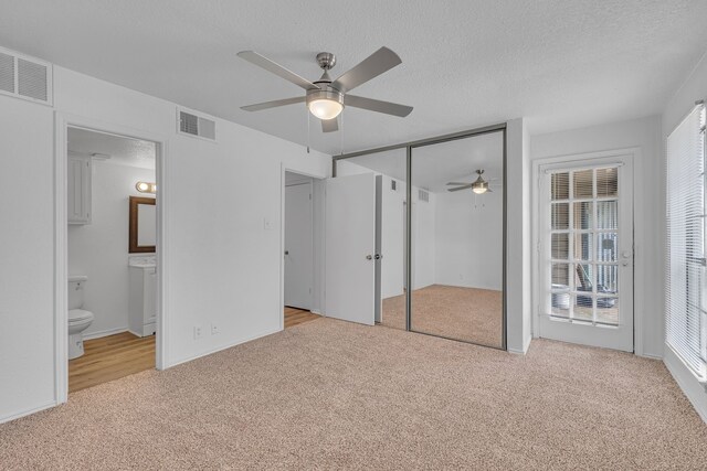 unfurnished bedroom with ceiling fan, ensuite bathroom, light colored carpet, and a textured ceiling