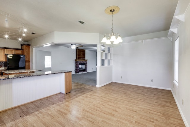 kitchen with a brick fireplace, light hardwood / wood-style flooring, dark stone countertops, pendant lighting, and black refrigerator