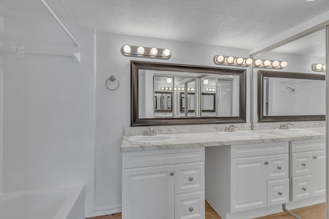 bathroom with vanity, a textured ceiling, and tiled shower / bath