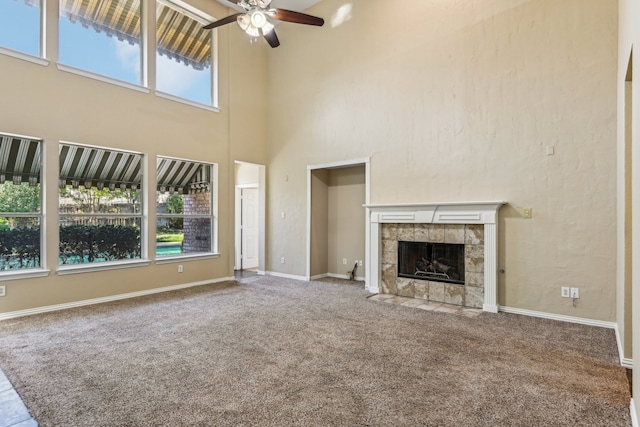 unfurnished living room with carpet flooring, ceiling fan, a fireplace, and a high ceiling