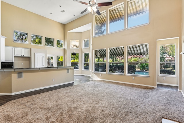 unfurnished living room with ceiling fan, dark hardwood / wood-style flooring, a healthy amount of sunlight, and a high ceiling