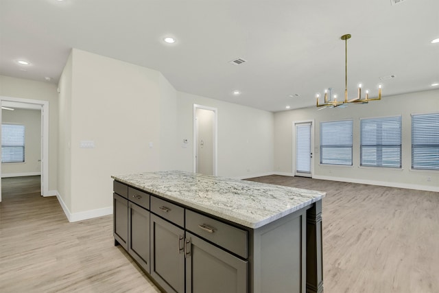 kitchen featuring gray cabinetry, light stone countertops, light hardwood / wood-style flooring, decorative light fixtures, and a kitchen island