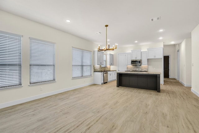 kitchen featuring a center island, light wood-type flooring, appliances with stainless steel finishes, decorative light fixtures, and white cabinetry