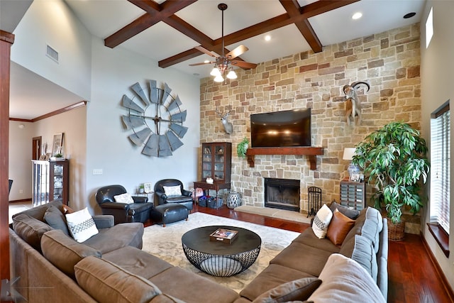 living room with ceiling fan, coffered ceiling, a stone fireplace, beamed ceiling, and wood-type flooring