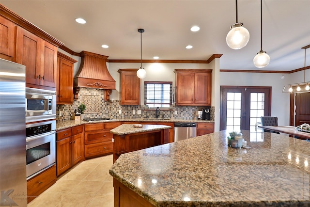 kitchen with appliances with stainless steel finishes, a wealth of natural light, custom exhaust hood, a kitchen island, and hanging light fixtures