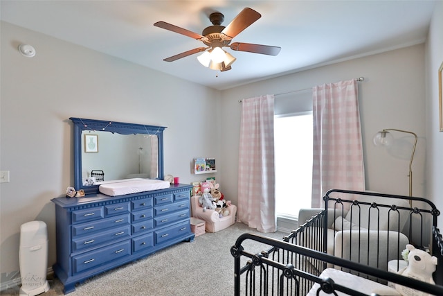 carpeted bedroom with ceiling fan and a nursery area