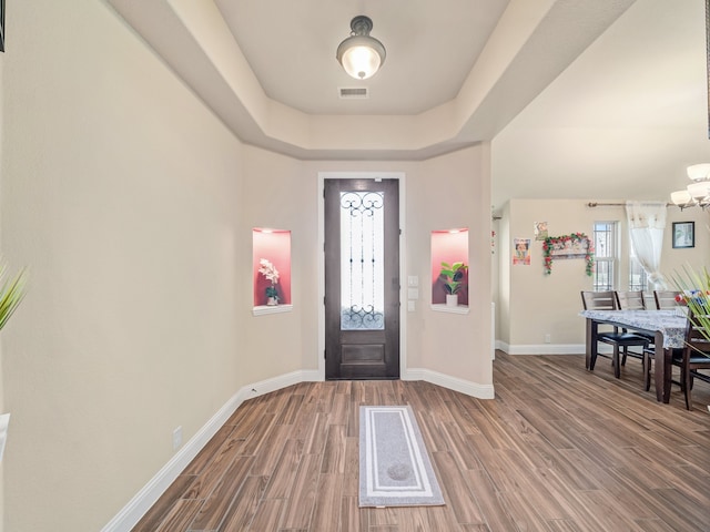 entryway featuring a raised ceiling, wood-type flooring, and an inviting chandelier