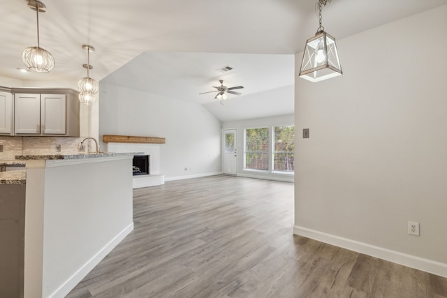 unfurnished living room featuring a brick fireplace, ceiling fan, sink, hardwood / wood-style flooring, and lofted ceiling