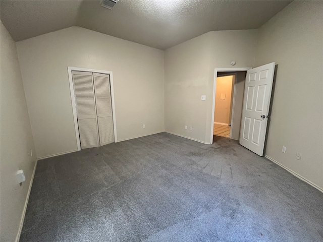 unfurnished bedroom with a textured ceiling, a closet, lofted ceiling, and dark colored carpet