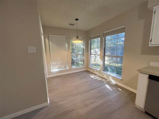 unfurnished dining area featuring a textured ceiling and light wood-type flooring