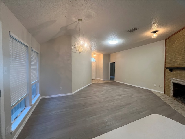 unfurnished living room with vaulted ceiling, a fireplace, a textured ceiling, dark hardwood / wood-style flooring, and a chandelier