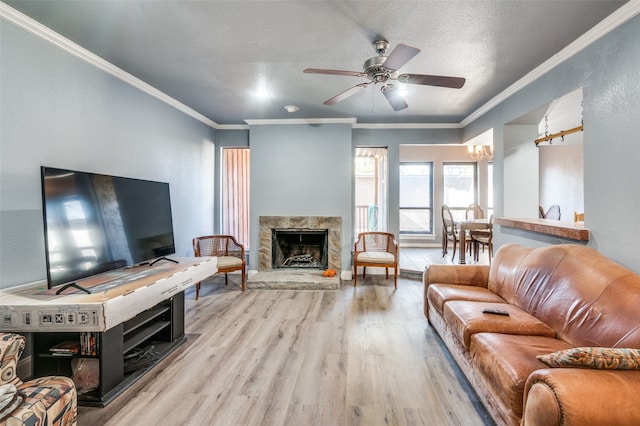 living room featuring a stone fireplace, light wood-type flooring, a textured ceiling, ceiling fan with notable chandelier, and ornamental molding