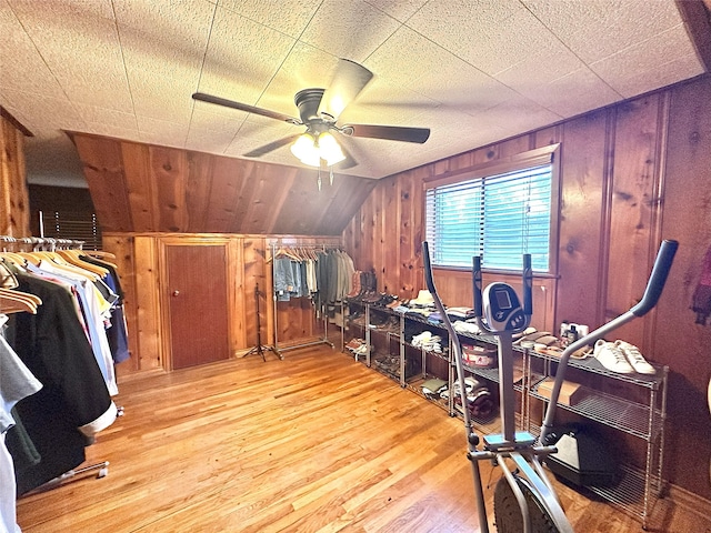 interior space featuring ceiling fan, wood walls, vaulted ceiling, and light wood-type flooring