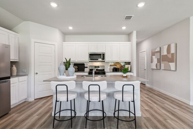 kitchen with stainless steel appliances, white cabinetry, and a kitchen island with sink