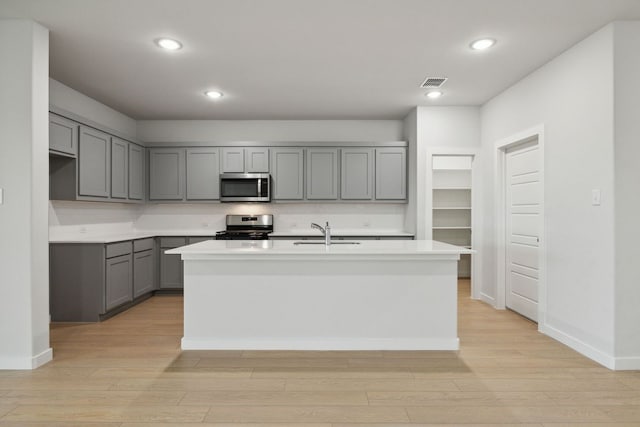 kitchen with gray cabinets, appliances with stainless steel finishes, a kitchen island with sink, and sink