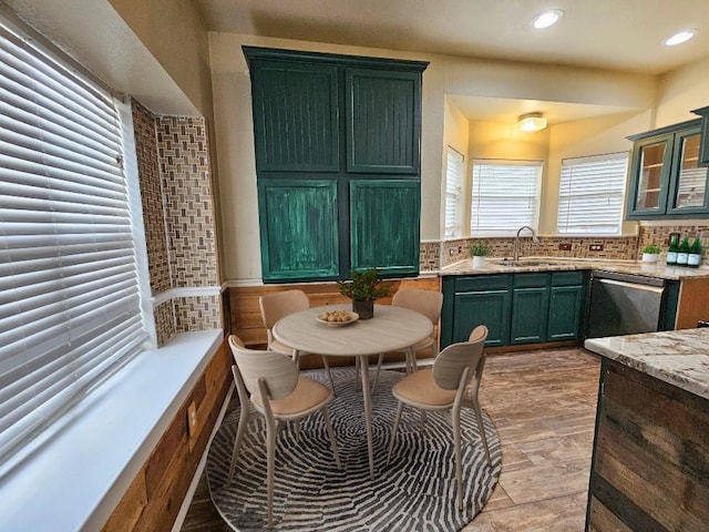 kitchen featuring backsplash, light stone counters, stainless steel dishwasher, sink, and green cabinetry