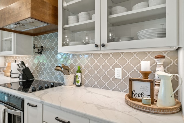 kitchen featuring tasteful backsplash, light stone counters, oven, black electric cooktop, and white cabinets