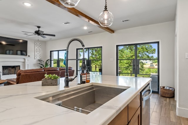 kitchen with light stone countertops, light wood-type flooring, stainless steel dishwasher, sink, and decorative light fixtures