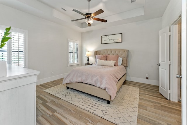 bedroom with a tray ceiling, ceiling fan, and light hardwood / wood-style flooring