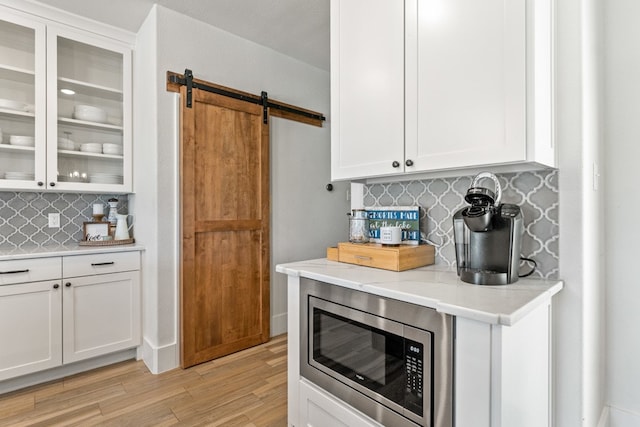 kitchen with stainless steel microwave, white cabinets, decorative backsplash, a barn door, and light hardwood / wood-style floors