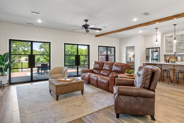 living room with beam ceiling, light hardwood / wood-style floors, ceiling fan, and sink