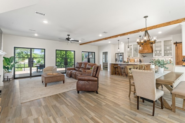 living room with ceiling fan with notable chandelier, light hardwood / wood-style floors, sink, and beam ceiling