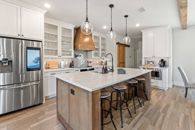 kitchen with a kitchen island with sink, white cabinets, sink, a barn door, and appliances with stainless steel finishes