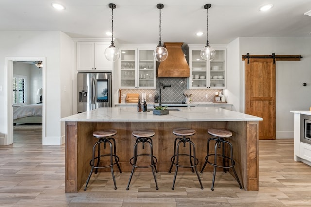 kitchen with white cabinetry, a barn door, stainless steel fridge with ice dispenser, a breakfast bar area, and a kitchen island with sink