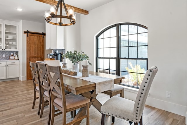 dining space featuring beam ceiling, a barn door, a notable chandelier, and light wood-type flooring