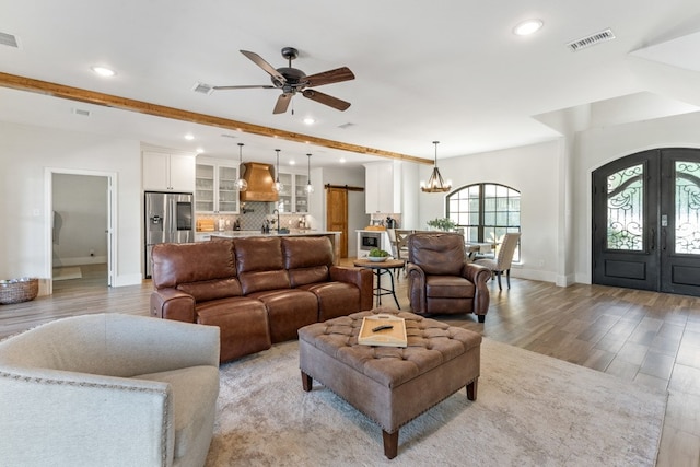 living room featuring french doors, ceiling fan with notable chandelier, and light wood-type flooring