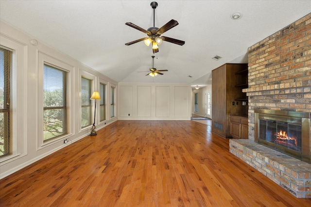 unfurnished living room featuring a textured ceiling, light wood-type flooring, a fireplace, and vaulted ceiling