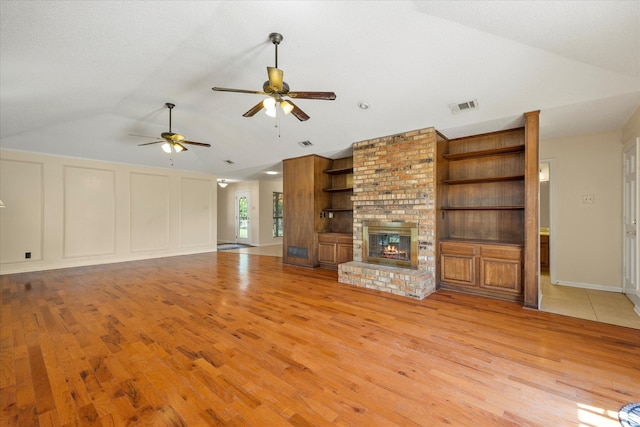 unfurnished living room with light wood-type flooring, a brick fireplace, ceiling fan, and vaulted ceiling