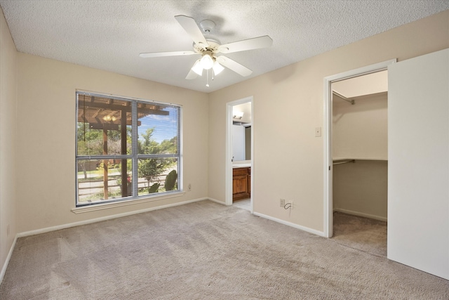 unfurnished bedroom featuring ceiling fan, a spacious closet, connected bathroom, light colored carpet, and a closet