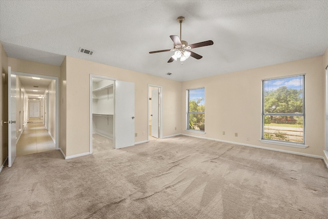 unfurnished bedroom featuring a spacious closet, ceiling fan, light colored carpet, and a textured ceiling