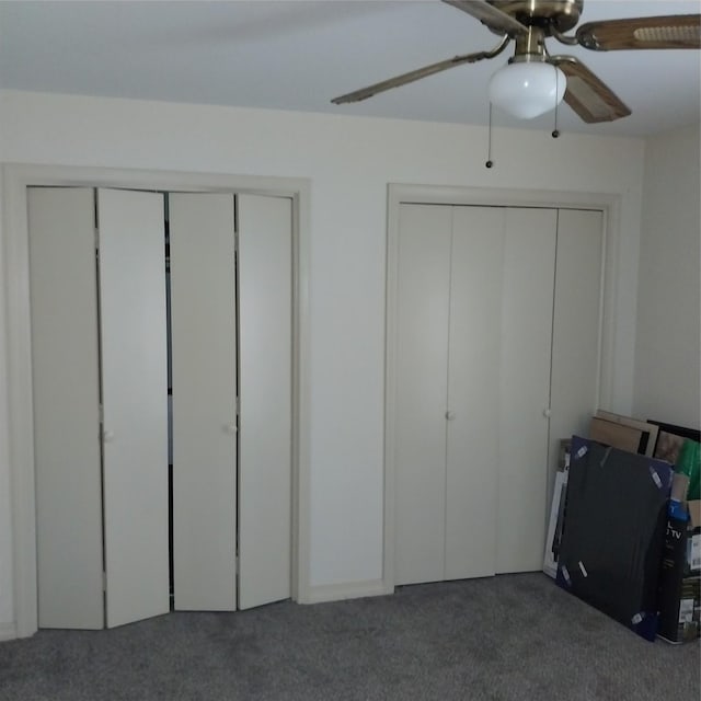 unfurnished bedroom featuring ceiling fan, dark carpet, and two closets