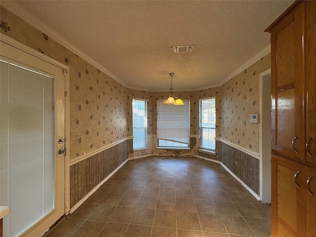 unfurnished dining area with dark tile patterned floors, ornamental molding, and a textured ceiling