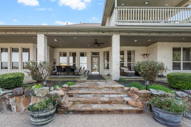 view of exterior entry featuring ceiling fan, a balcony, and a patio