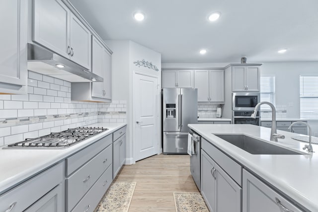 kitchen with gray cabinetry, sink, stainless steel appliances, light hardwood / wood-style flooring, and decorative backsplash