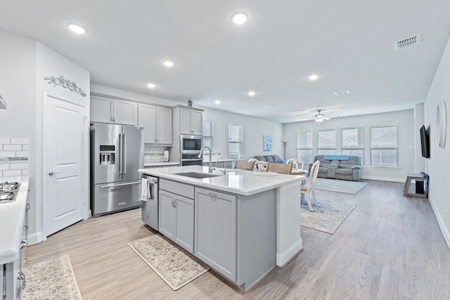 kitchen with an island with sink, stainless steel appliances, gray cabinets, and sink