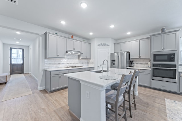 kitchen with sink, an island with sink, stainless steel appliances, and light wood-type flooring