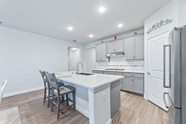 kitchen with appliances with stainless steel finishes, light wood-type flooring, sink, a center island with sink, and gray cabinets