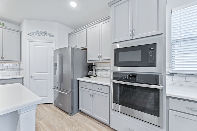 kitchen featuring gray cabinetry, backsplash, appliances with stainless steel finishes, and light hardwood / wood-style flooring