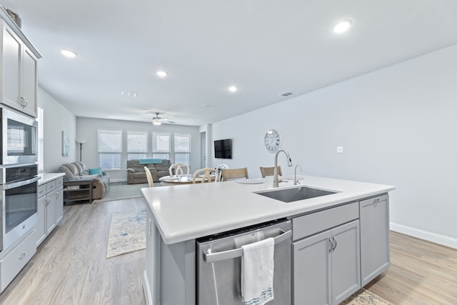 kitchen featuring a kitchen island with sink, sink, light wood-type flooring, and appliances with stainless steel finishes