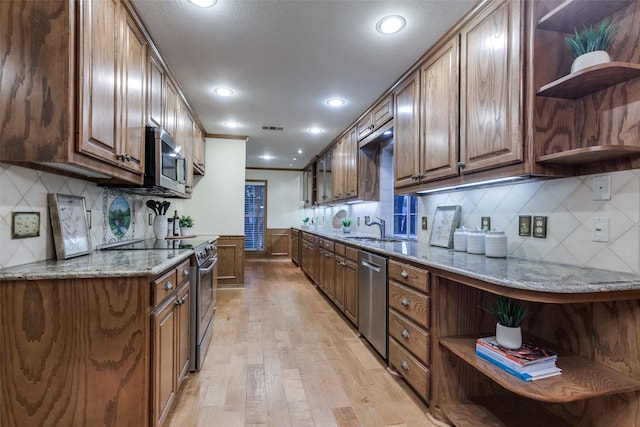 kitchen featuring sink, appliances with stainless steel finishes, light stone counters, tasteful backsplash, and light wood-type flooring