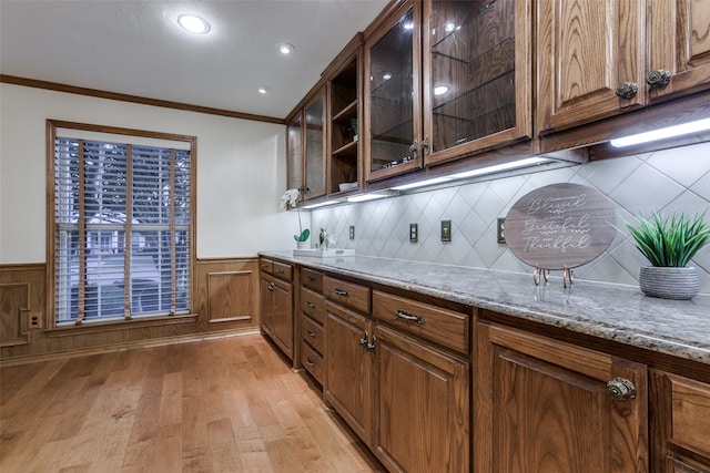 bar with backsplash, sink, crown molding, light stone countertops, and light wood-type flooring