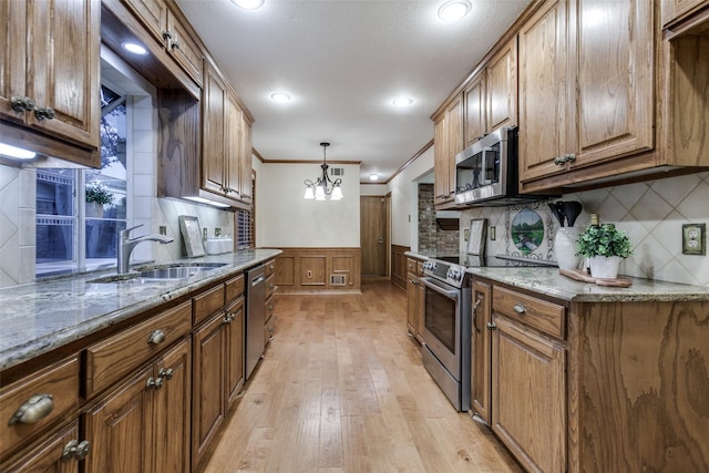 kitchen with sink, stainless steel appliances, ornamental molding, light stone countertops, and decorative light fixtures