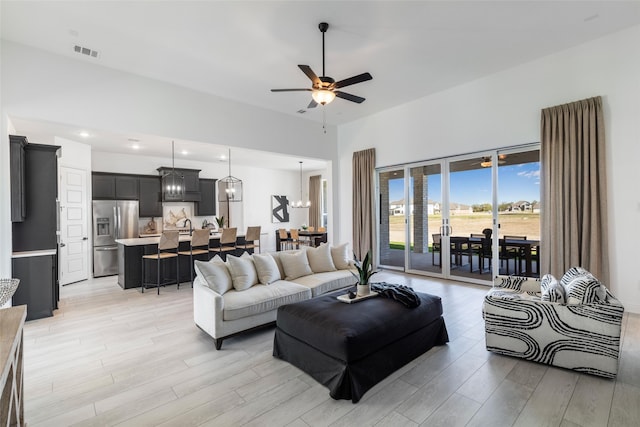 living room featuring ceiling fan with notable chandelier and light hardwood / wood-style flooring