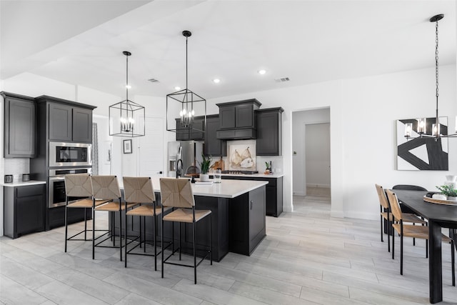 kitchen with backsplash, an island with sink, hanging light fixtures, and appliances with stainless steel finishes