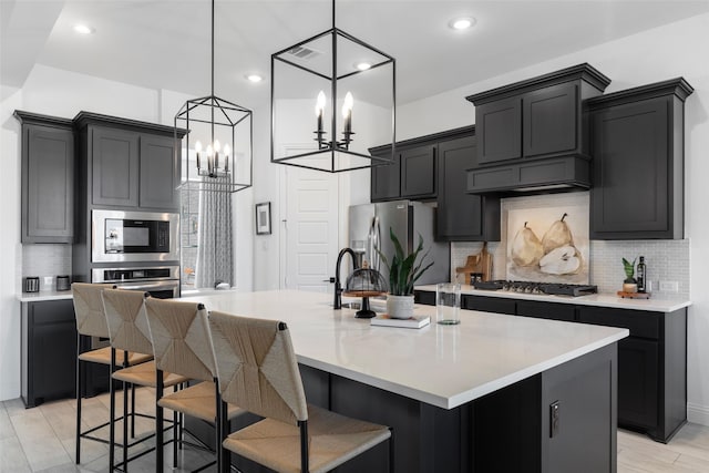 kitchen with pendant lighting, a center island with sink, stainless steel appliances, and light wood-type flooring