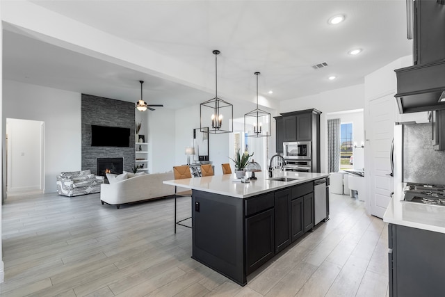 kitchen featuring sink, ceiling fan, a fireplace, an island with sink, and stainless steel appliances